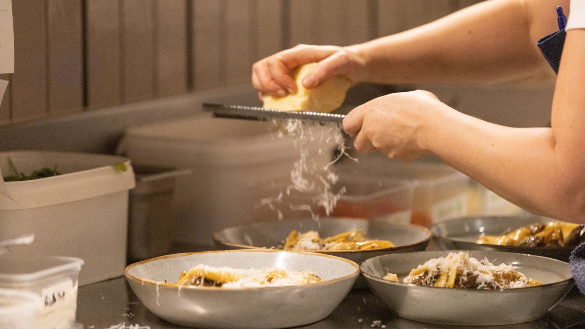 A chef grating fresh parmesan over bowls of pasta on the pass at Earl